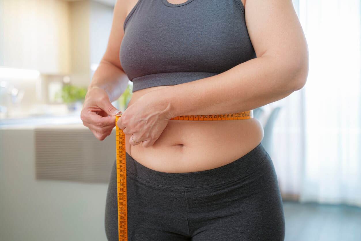 Mulher plus size medindo sua cintura com fita métrica